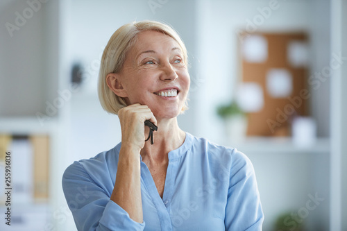 Cheerful mature blonde female with toothy smile looking aside during working day in office