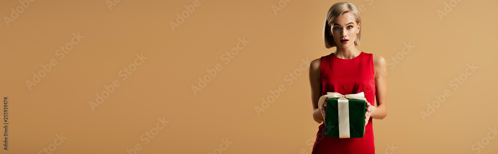 panoramic shot of surprised and beautiful young woman in red dress holding gift box isolated on beige panoramic shot of surprised and beautiful young woman in red dress holding gift box isolated on beige