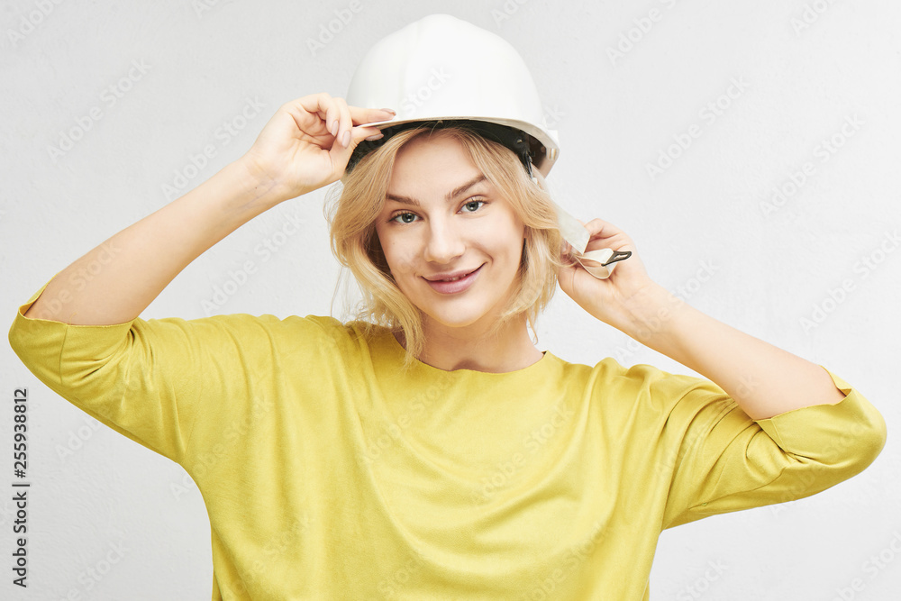 Portrait of young sexy blond woman engineer in construction helmet posing, gently smiling at camera isolated on white background in studio Portrait of young sexy blond woman engineer in construction helmet posing, gently smiling at camera isolated on white background in studio