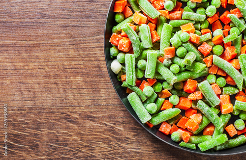 Mixed vegetables. green beans, peas and carrots in an iron pan on a wooden background