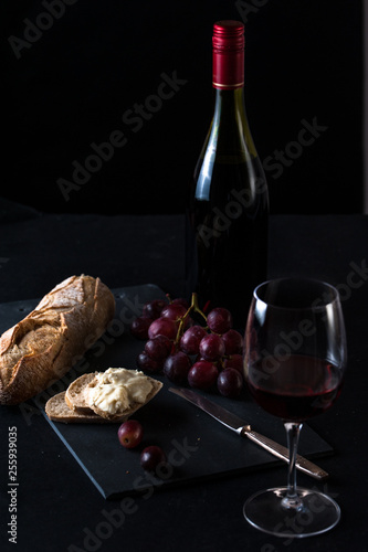 glass of red wine,  a wine bottle, cheese board with a cluster of grapes, brie cheese, rustick bread and antique knife. photo