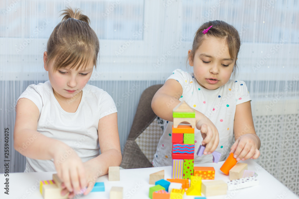 Fototapeta premium Children play with an educational toy on table in the children's room. Two kids playing with colorful blocks. Kindergarten educational games
