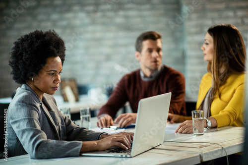 Black female bank manager working on laptop while having meeting with a couple.