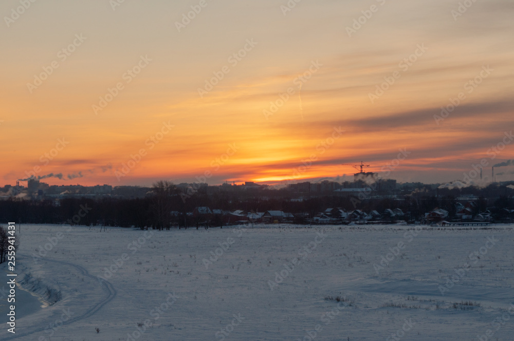Winter sunrise at the river cliffs with the river encased in ice, snowed plains and a city in the distance