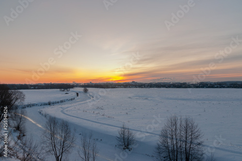 Winter sunrise at the river cliffs with the river encased in ice  snowed plains and a city in the distance