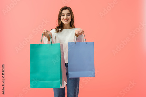 smiling woman in white sweater and jeans holding shopping bags isolated on pink