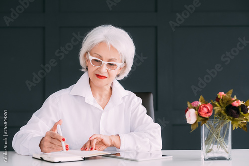 Senior business woman portrait. Day planning. Elderly lady at workplace making notes in day planner. photo