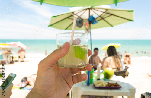 Relax time at the beach in Marataizes, a little seaside village in the Espirito Santo state in Brazil. A hand holding a caipirinha a typical local drink