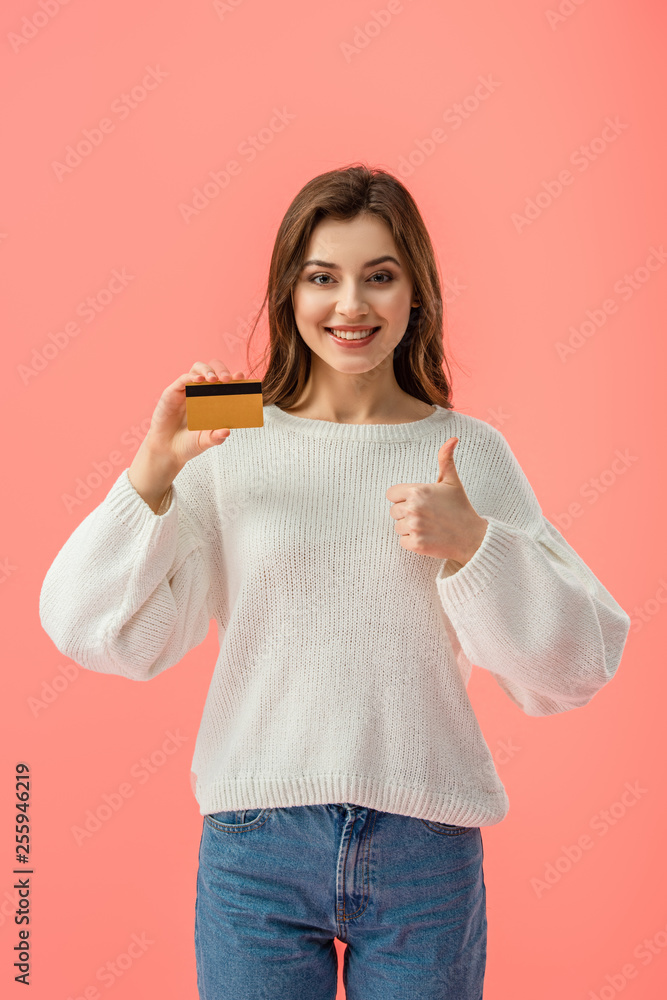 smiling brunette girl holding credit card and showing thumb up isolated on pink smiling brunette girl holding credit card and showing thumb up isolated on pink
