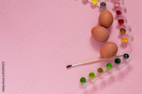 Closeup easer eggs on pink background with paints for decorating. Preparing for religious holiday in spring. Hello april.