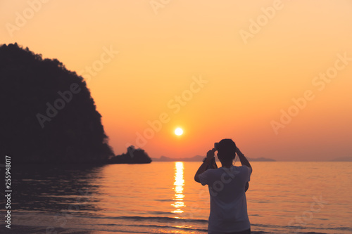 Woman taking a picture in sunset time at beach.