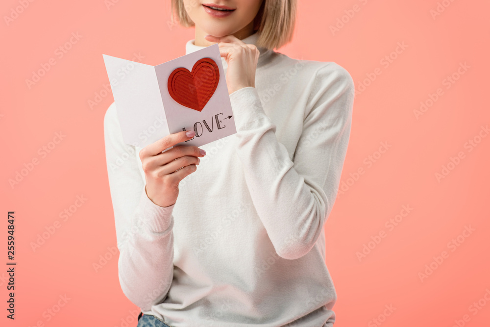 cropped view of woman holding greeting card while standing isolated on pink cropped view of woman holding greeting card while standing isolated on pink
