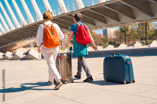 Two mid age woman caring luggage. Rear view, stylish travelers with colorful backpacks.