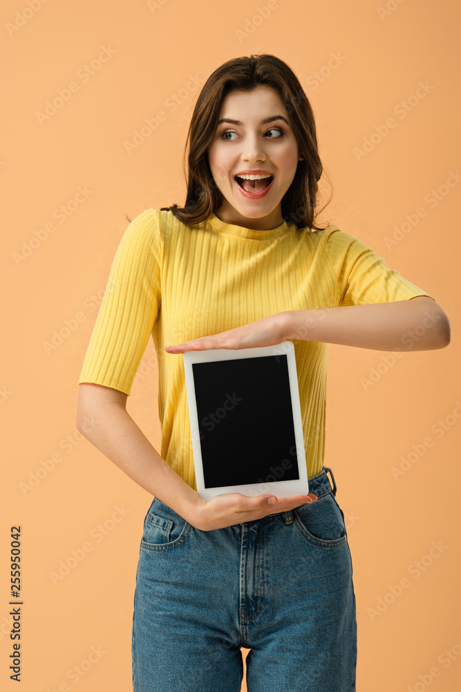 Excited young woman holding digital tablet with blank screen isolated on orange Excited young woman holding digital tablet with blank screen isolated on orange