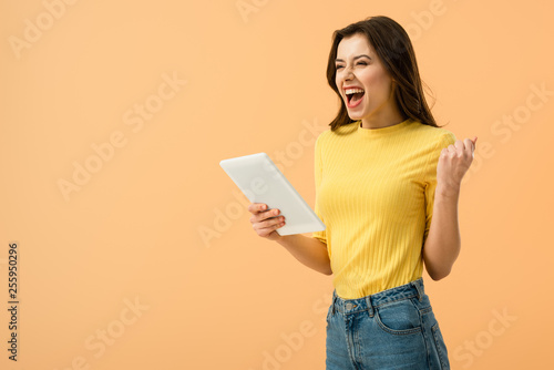 Excited brunette girl holding digital tablet and laughing isolated on orange