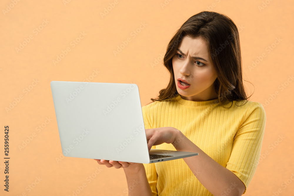Dissatisfied brunette young woman using laptop isolated on orange Dissatisfied brunette young woman using laptop isolated on orange