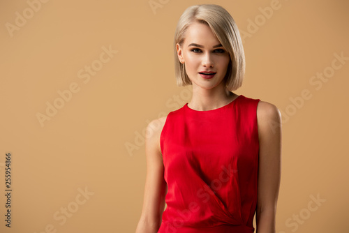 Stylish blonde young woman in red dress looking at camera isolated on beige © LIGHTFIELD STUDIOS