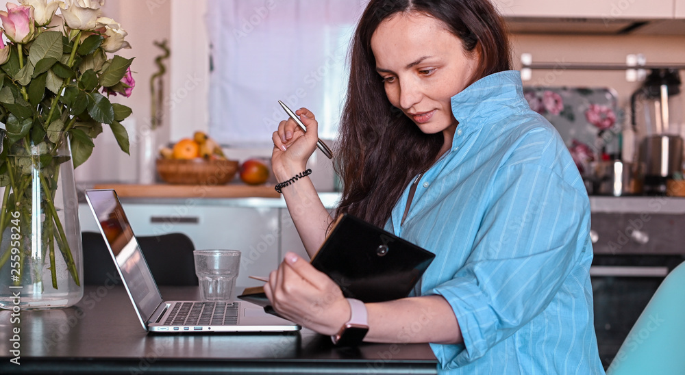 Young beautiful woman working at home at the computer. Home office for remote work. Business lady in a comfortable house and flowers on the table. Free space for text Young beautiful woman working at home at the computer. Home office for remote work. Business lady in a comfortable house and flowers on the table. Free space for text