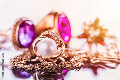 Elegant luxury composition of gold jewelry with pearl ring, amethysts and rubys gemstones on light background close-up macro and reflection