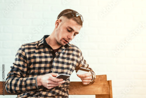 a young guy with a phone and a credit card on a bench in the room © komokvm