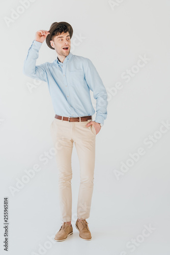 happy handsome man in blue shirt and beige jeans with hand in pocket isolated on grey