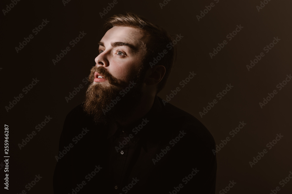 Sepia portrait of a pensive man with a beard and stylish hairdo dressed in the black shirt on the dark background