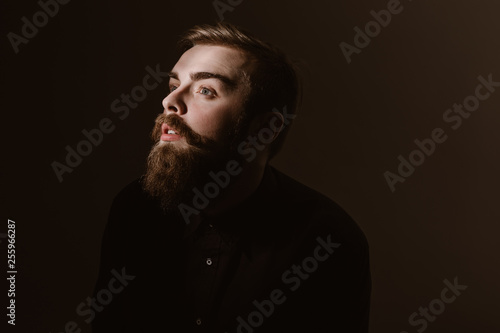 Sepia portrait of a pensive man with a beard and stylish hairdo dressed in the black shirt on the dark background