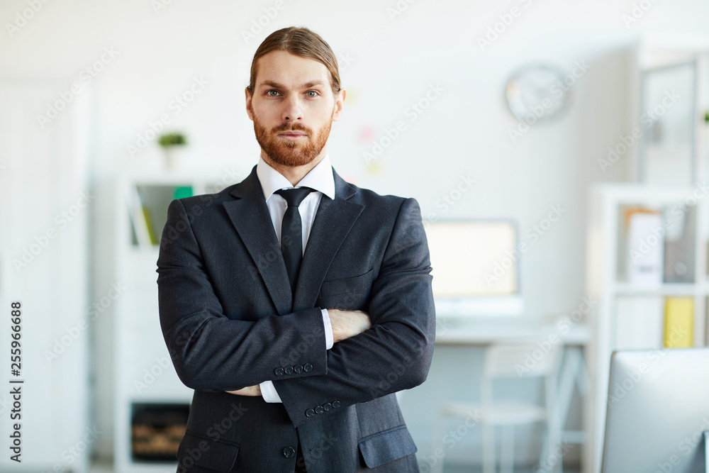 Young bearded business employee in elegant suit crossing arms on chest while standing in front of camera Young bearded business employee in elegant suit crossing arms on chest while standing in front of camera