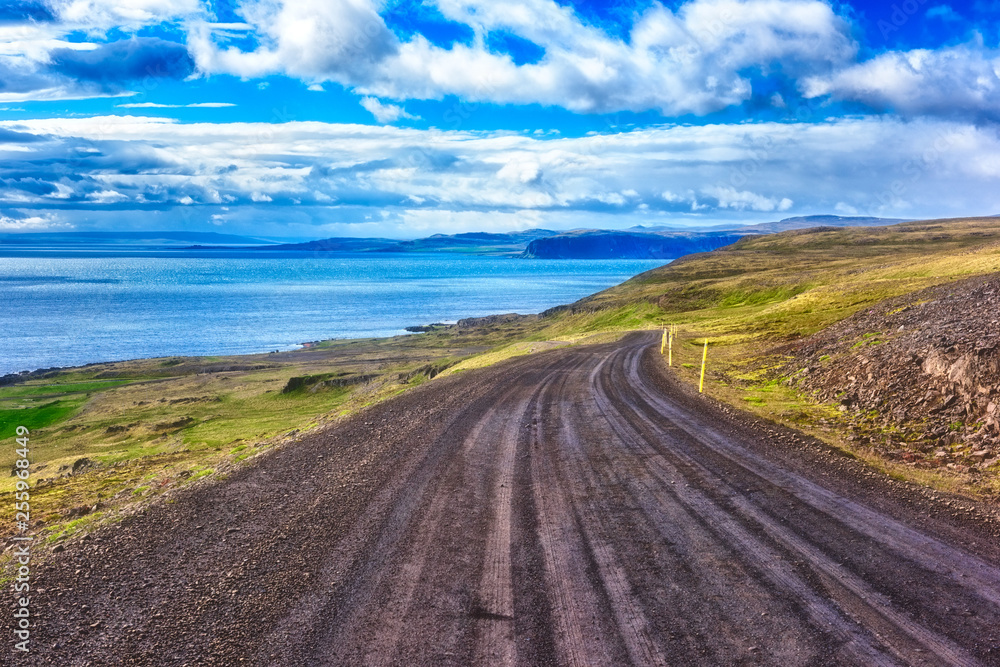 Winding dirt road along the Atlantic coast of Iceland. Bright daytime landscape with amazing blue sky, the way to the Latrabjarg, the westernmost point in Iceland, outdoor travel background