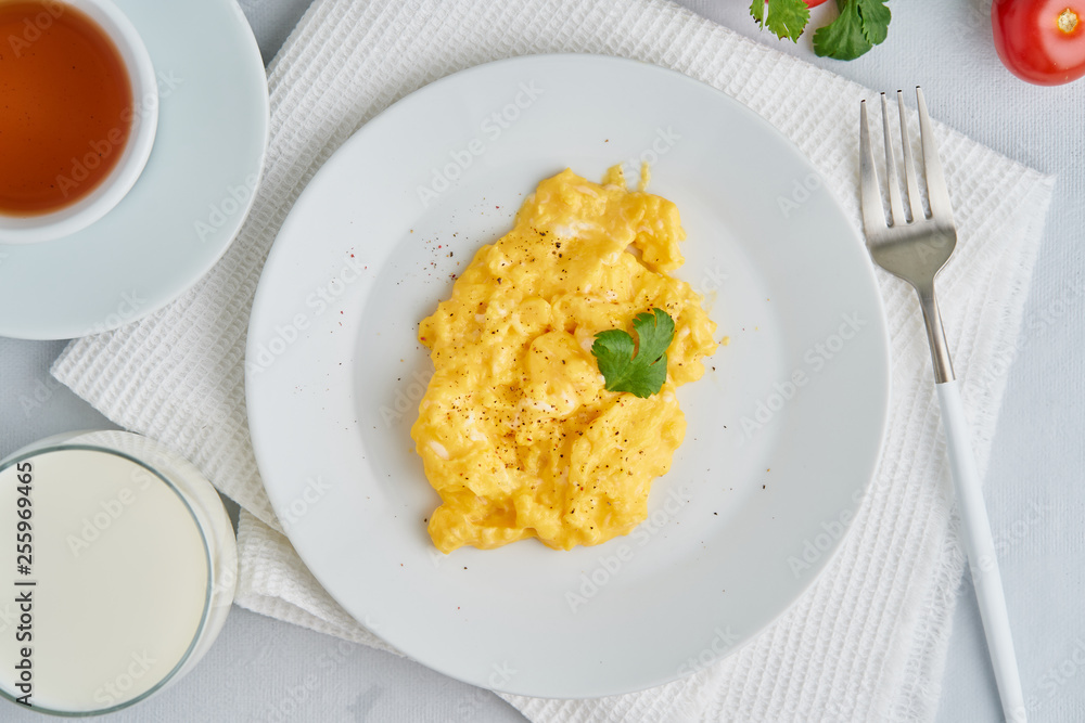 Breakfast with pan-fried scrambled eggs, cup of tea, tomatoes on white background. Omelette, top view