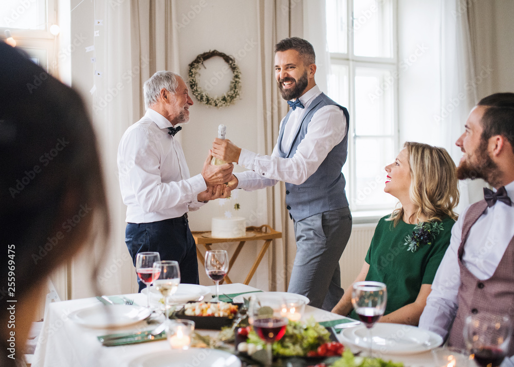 A man giving a bottle of wine to his father on indoor birthday party, a celebration concept. A man giving a bottle of wine to his father on indoor birthday party, a celebration concept.