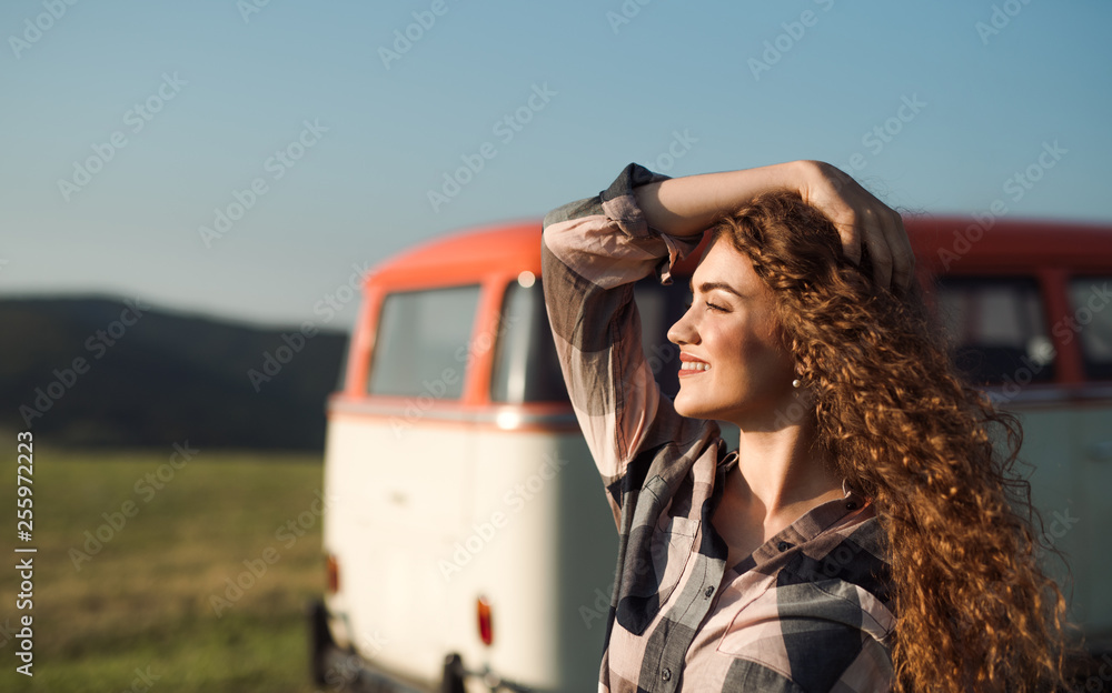 A young girl on a roadtrip through countryside, standing by a minivan.