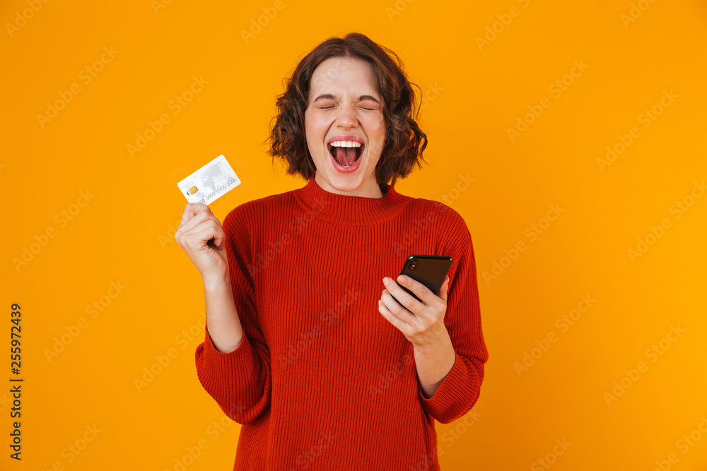 Portrait of attractive woman using cell phone and credit card while standing isolated over yellow background Portrait of attractive woman using cell phone and credit card while standing isolated over yellow background