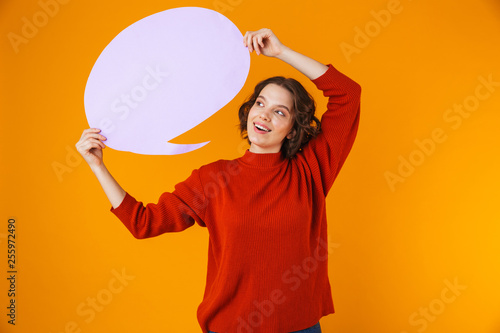 Image of cheerful girl holding thought bubble with copyspace while standing isolated over yellow background © Drobot Dean