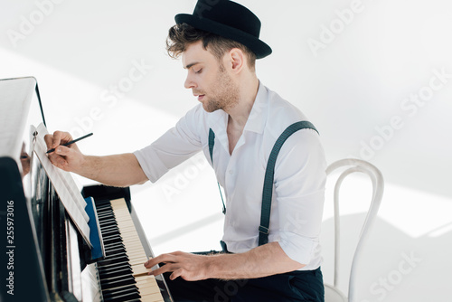 Foto focused composer writing in music book and playing piano