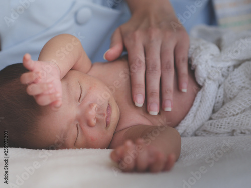 Mother take care of Asian female newborn baby lying in bed and sunlight in the morning. Cute little girl three weeks old. Healthcare, love, relationship concept
