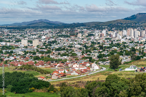 View from a mountain of a grove, the city of Tandil and a mountain range on the back with a few clouds on the sky