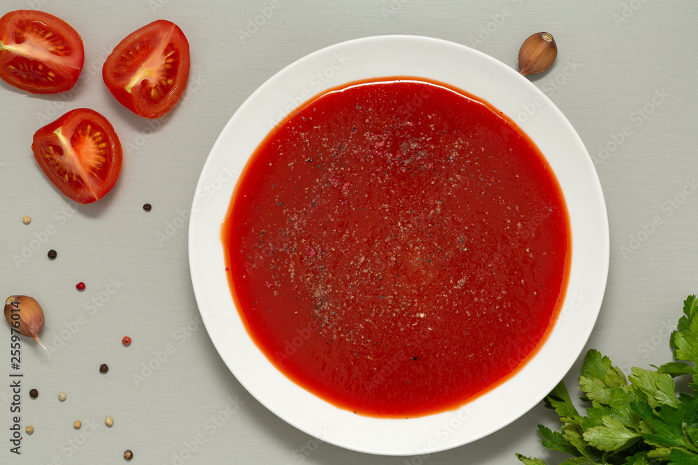 Tomato soup in a white bowl on grey background. Delicious soup of tomatoes and fresh herbs with garlic and spices. Top view. Tomato soup in a white bowl on grey background. Delicious soup of tomatoes and fresh herbs with garlic and spices. Top view.