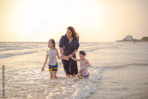 Mother and children playing on the beach at the sunset time. Concept of happy family