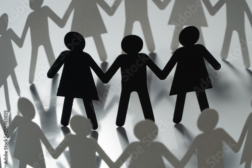 Papier peint Three human paper figures surrounded by circle of paper people holding hands on white surface