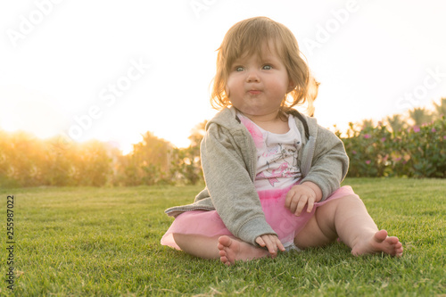 Funny little girl sitting on grass on vacation
