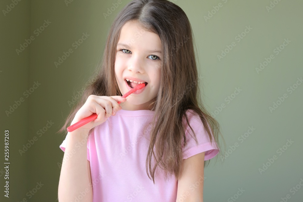 Girl brushing her teeth. Long haired smiling beautiful caucasian white girl brushing teeth with pink toothbrush on green background. Green eyed cute child in pink tshirt doing her morning hygiene. Girl brushing her teeth. Long haired smiling beautiful caucasian white girl brushing teeth with pink toothbrush on green background. Green eyed cute child in pink tshirt doing her morning hygiene.