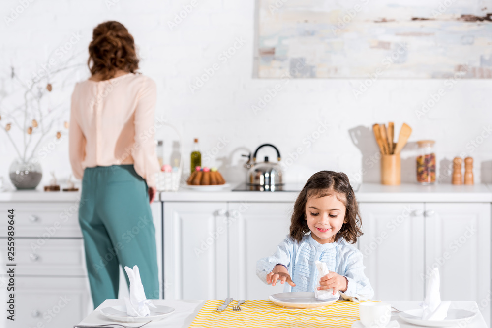 Smiling preschooler kid folding napkin at table in kitchen Smiling preschooler kid folding napkin at table in kitchen