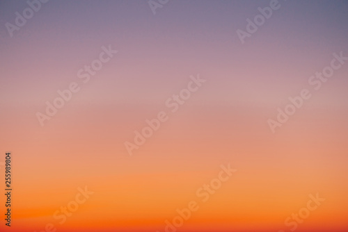 Predawn clear sky with orange horizon and violet atmosphere. Smooth orange violet gradient of dawn sky. Background of day beginning. Heaven at early morning with copy space. Sunset, sunrise backdrop