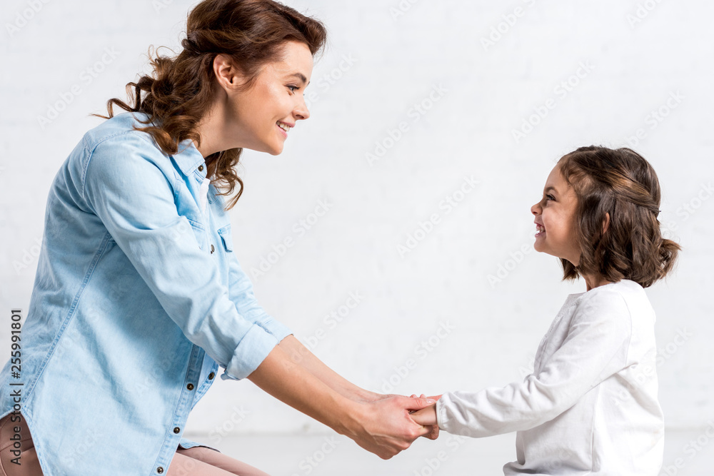 Happy mother and kid holding hands and looking at camera on white Happy mother and kid holding hands and looking at camera on white