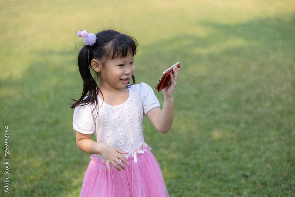 children thai girl standing are watching cartoon movies on smartphone with high-speed 4G WI-FI system in the garden Greenland children thai girl standing are watching cartoon movies on smartphone with high-speed 4G WI-FI system in the garden Greenland