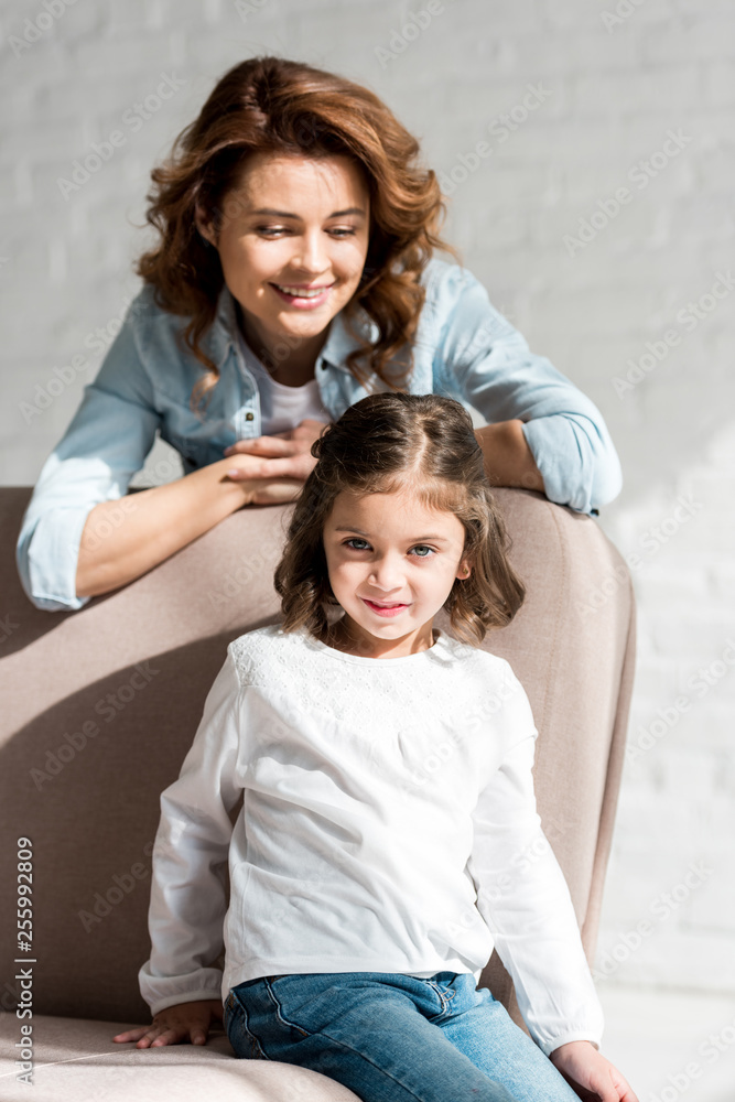 Smiling mother and daughter sitting on sofa and using smartphone Smiling mother and daughter sitting on sofa and using smartphone