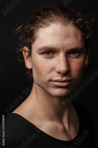 Portrait of a handsome long-haired man with drawn hair and freckles wearing a black T-shirt