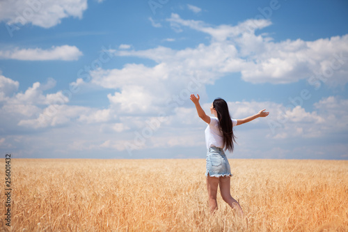 Happy woman enjoying the life in the field Nature beauty  blue sky and field with golden wheat. Outdoor lifestyle. Freedom concept. Woman jump in summer field