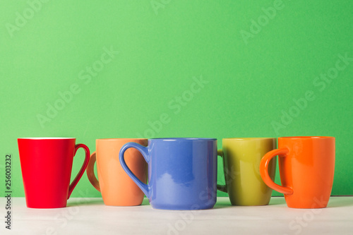 A lot of multicolored cups of coffee or tea on a green background. The concept of a friendly company, a large family, meeting friends for a cup of tea or coffee.